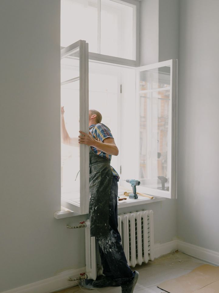 Handyman fitting a tall window sash in a bright room