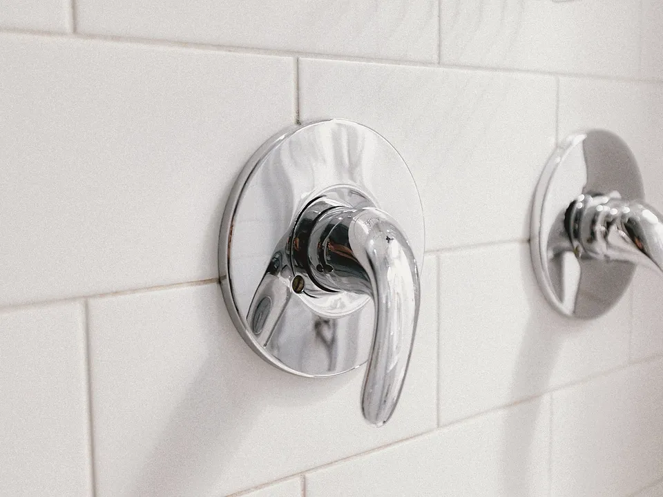 Chrome shower valve handles on a white tile wall