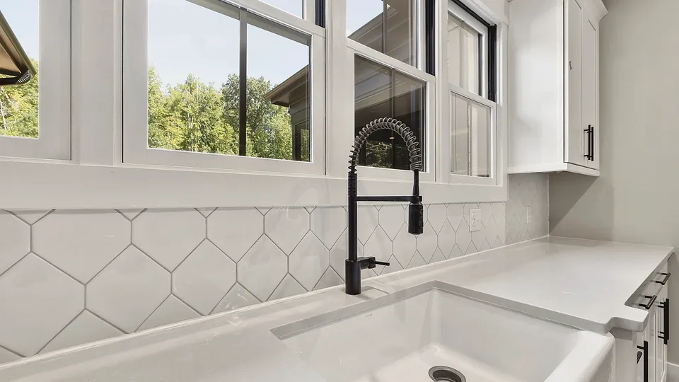 White kitchen sink with a black faucet under a window