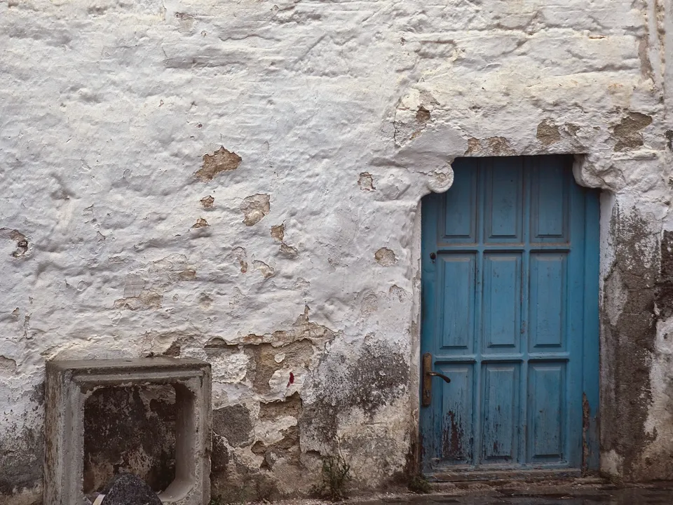 Old whitewashed plaster wall with a blue wood door