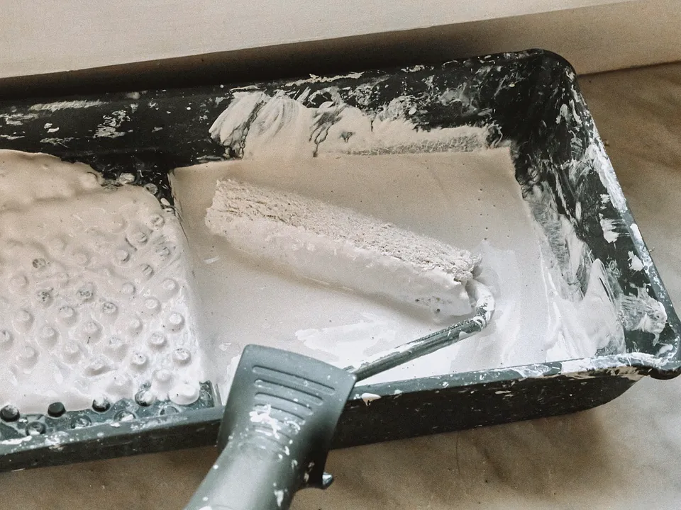 Roller and brush resting in a tray of white primer