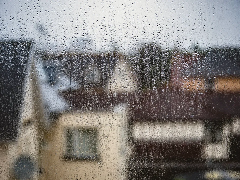 Rain-streaked window with a house blurred behind it