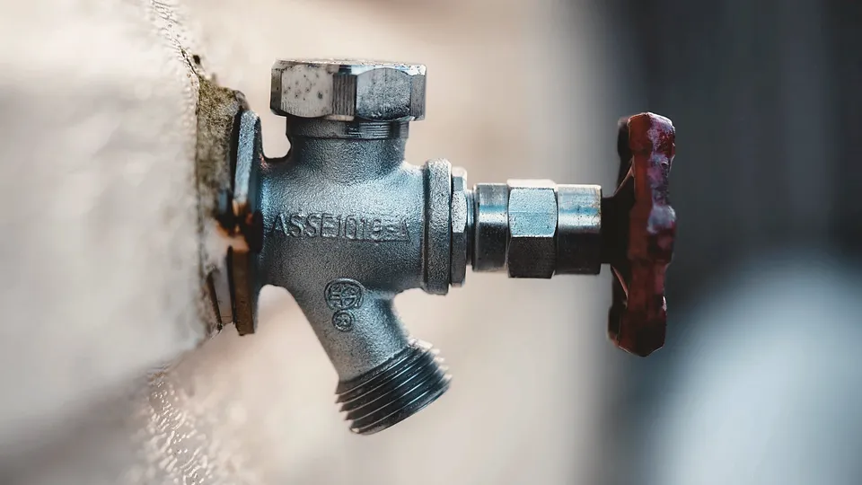 Brass shutoff valve with a red handle on a wall