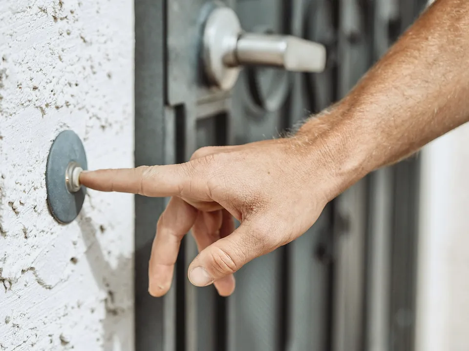 Finger pressing a doorbell button on a textured wall