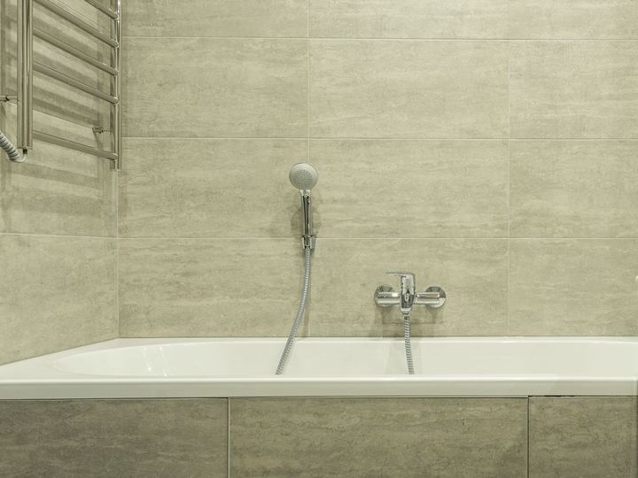 White built-in bathtub with a hand shower against large beige wall tiles