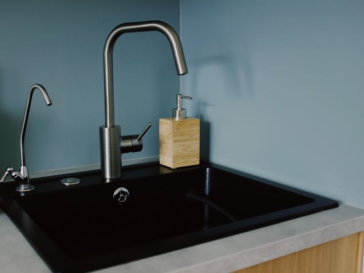 Black kitchen sink with a brushed steel faucet and a filtered water tap against a blue wall