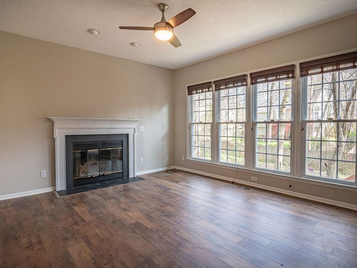 Ceiling fan with a light kit above an empty living room with a fireplace and tall multi-pane windows