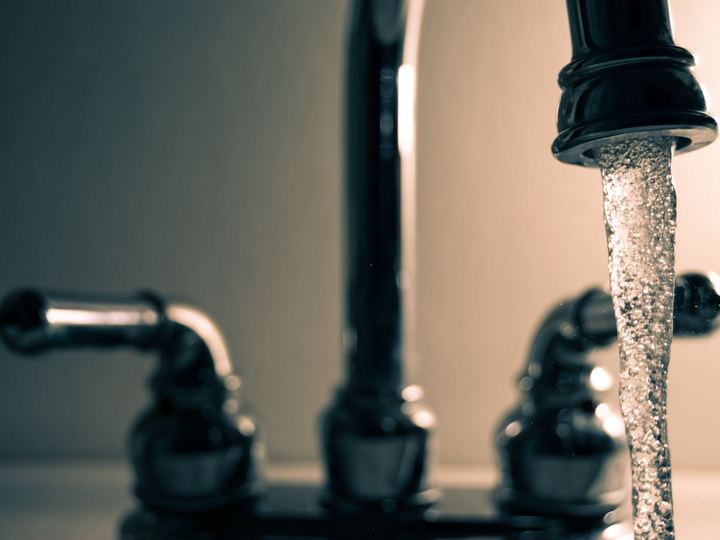 Water running from a dark two-handle faucet with lever handles
