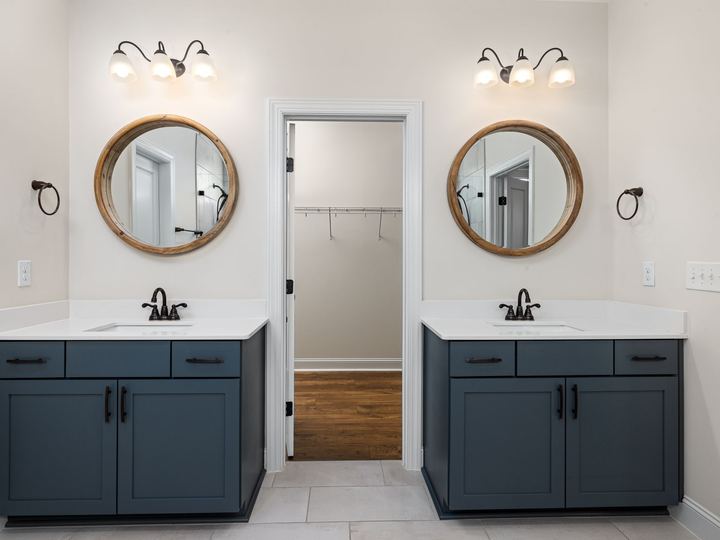 Two vanities with round wood-framed mirrors, each under a three-globe bronze vanity light