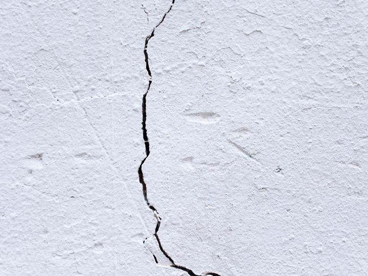 Close-up of a long crack running down a white textured plaster wall