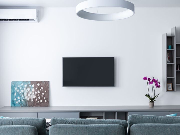 Flat-screen TV mounted on a plain white living room wall above a low gray console