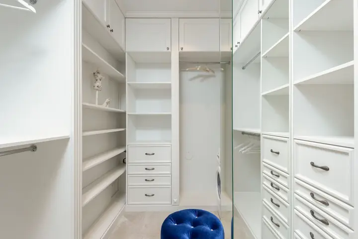 White closet with shelves and drawers and a blue stool