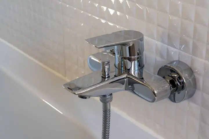 Chrome tub faucet on white textured wall tiles