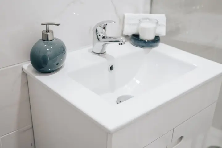 Chrome faucet and blue soap pump on a white sink