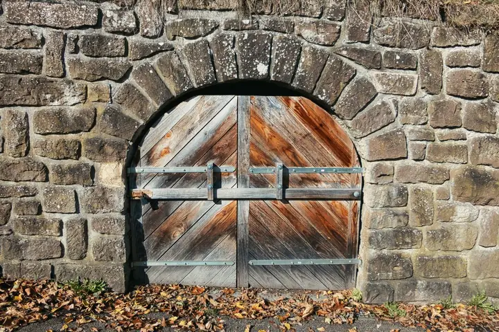 Rustic wooden gate set in a stone archway, surrounded by autumn leaves