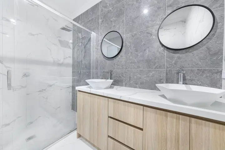 Two vessel sinks on a wood vanity under oval mirrors
