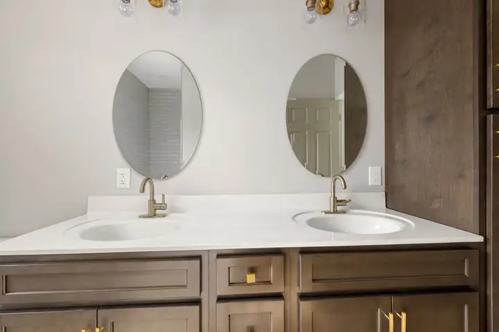 Two oval mirrors over a white double vanity with brass faucets