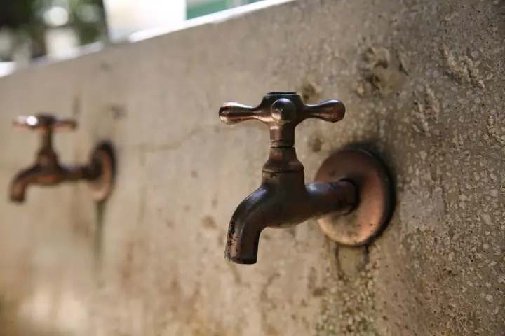Two old brass outdoor faucets on a rough concrete wall