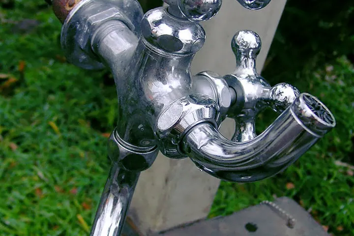 Chrome outdoor faucet with cross handles on a post in a garden
