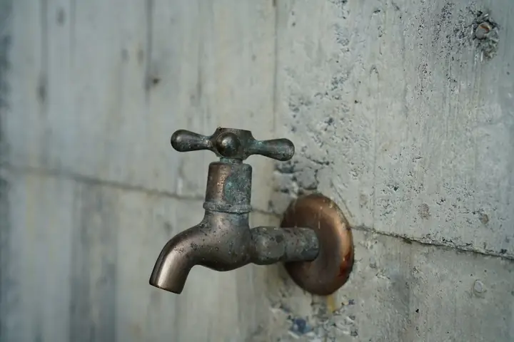 Old metal outdoor faucet on a gray concrete wall