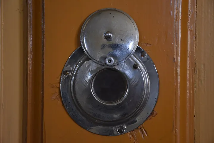 Old peephole with a swing cover on a wooden door