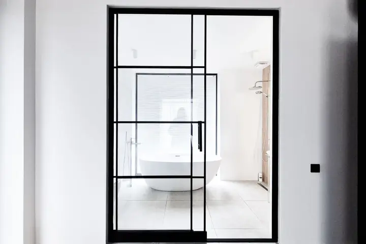 Black framed glass door opening to a bathroom with a tub