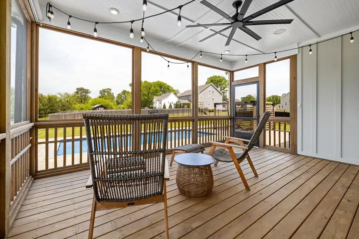 Screened porch with a ceiling fan and chairs facing a pool