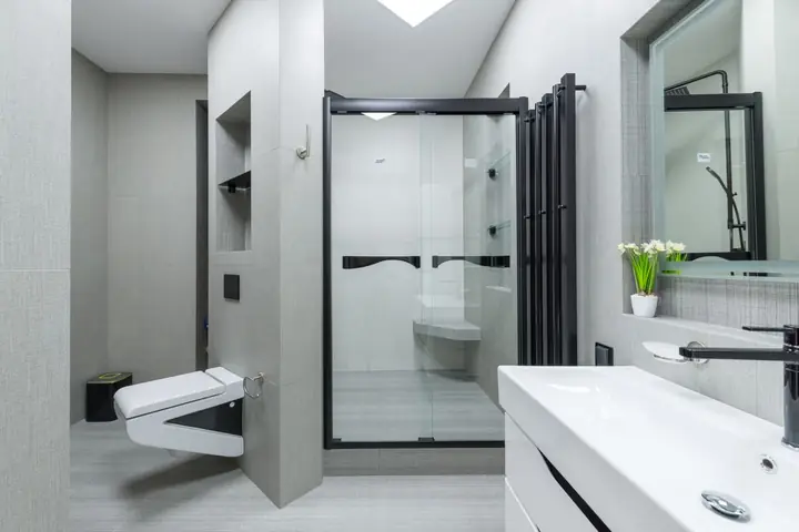 Glass shower, wall toilet and white vanity in a gray bathroom