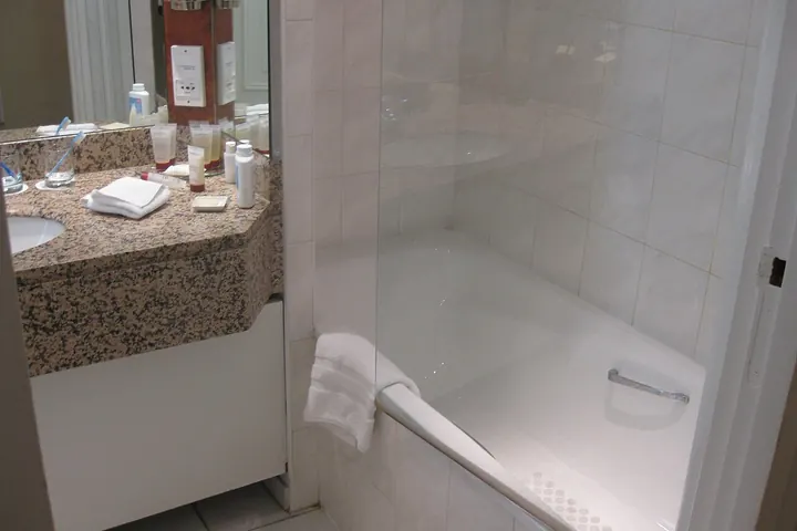 White bathtub with a grab bar beside a stone vanity