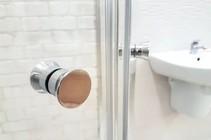 Chrome knob on a glass shower door beside a white sink