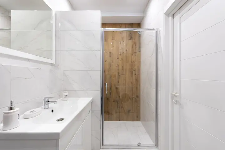 White vanity facing a shower with a wood look tile wall