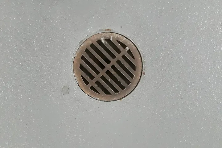 Round metal drain grate in a pale floor