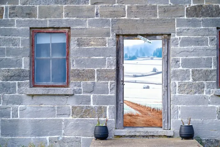 Old stone building's door frame reveals a tranquil winter landscape view