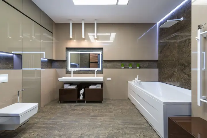 Wall toilet, tub and lit mirror in a beige bathroom