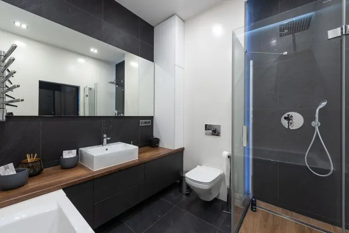 Glass shower beside a wall toilet and a dark vanity