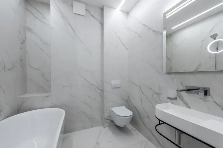 White tub, wall toilet and floating sink in a marble bathroom