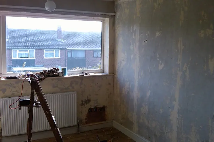 Room stripped of wallpaper with a stepladder under the window